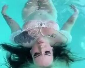 Goth girl floats in the pool with her tits out